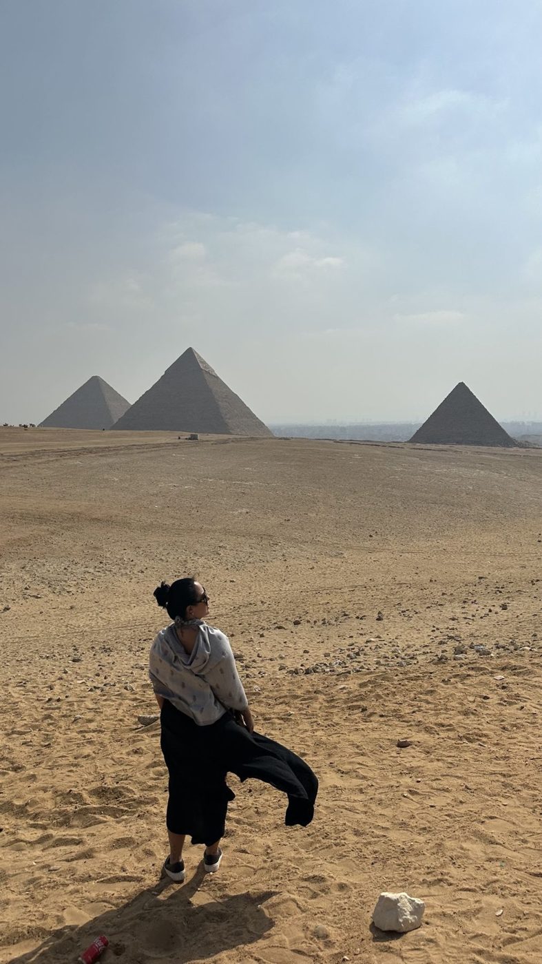 Pirâmides de Gizé no horizonte, mulher de costas no deserto